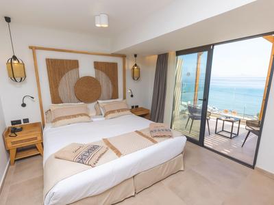 Modernes Hotelzimmer mit Doppelbett, seitlichen Nachttischen und Meerblick durch große Glasfenster.