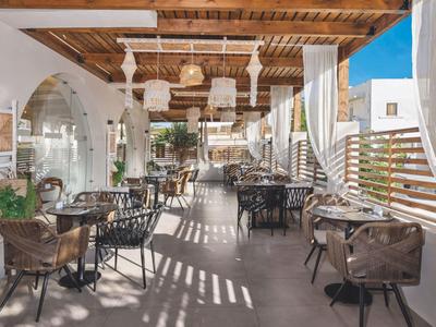 Hell beleuchtete gedeckte Terrasse mit Tisch- und Stuhlarrangements und Holzbalkendecke.