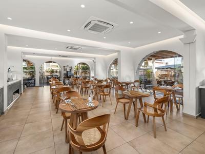 Helles Restaurant mit Holztischen und Stühlen, großen Fenstern und modernen weißen Wänden.