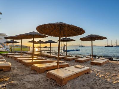 Strand met houten ligbedden en strooien parasols bij zonsondergang aan zee.