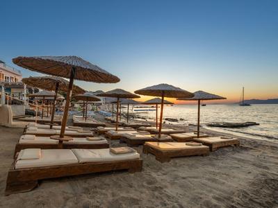 Meerdere ligbedden met strooien parasols op het zandstrand bij zonsondergang.
