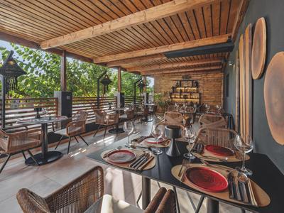 Überdachter Außenbereich eines Restaurants mit Holzdach und gedeckten Tischen neben einer Steinwand.