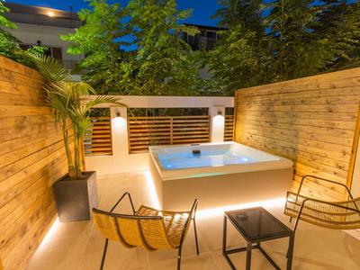 Verlicht bubbelbad op houten terras met twee stoelen en vierkante tafel 's nachts