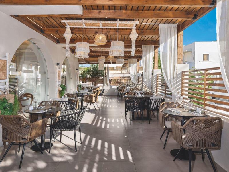 Lichte buitenterras met houten plafondbalken, tafels en stoelen onder natuurlijk licht.