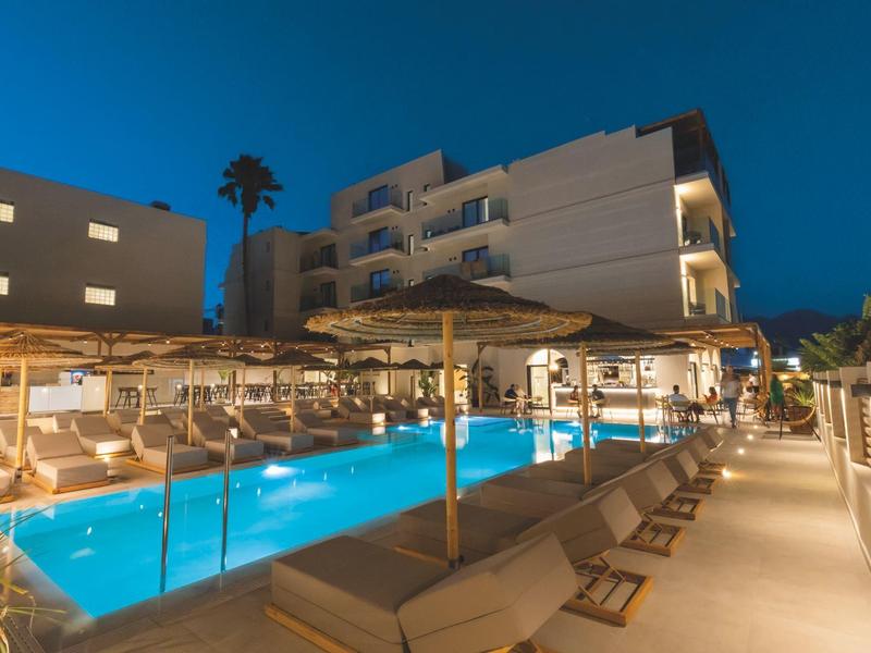 Verlicht hotelzwembad met ligstoelen en palmbomen in de avond