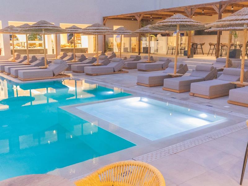 Modern buitenzwembad met ligstoelen en parasols bij een hotelresort tijdens zonsondergang.