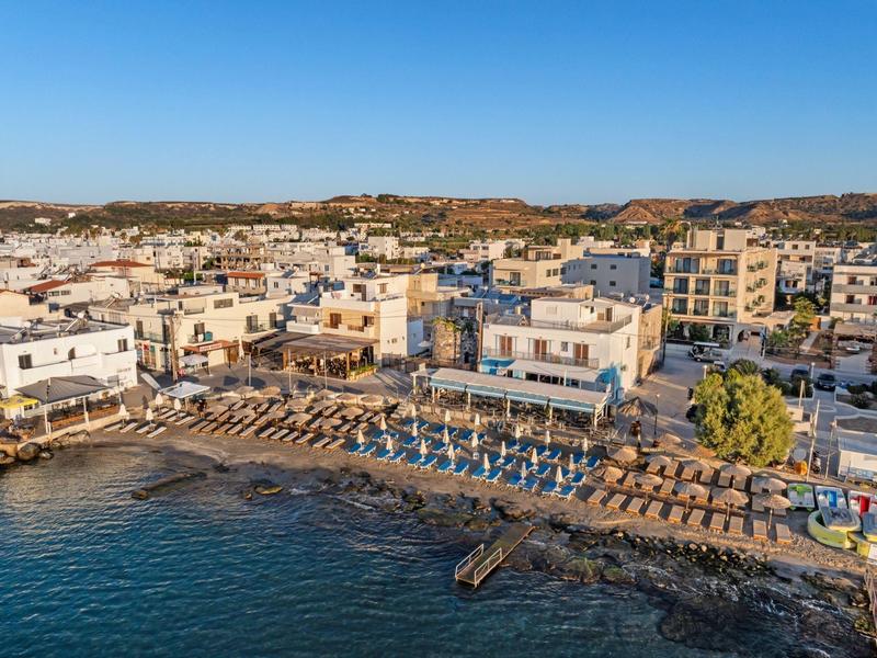 Uitzicht op een kustplaats met strand, parasols en gebouwen onder een heldere hemel.
