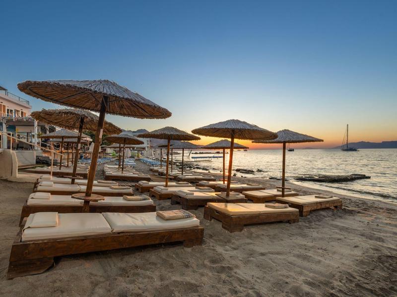 Meerdere ligbedden met strooien parasols op het zandstrand bij zonsondergang.