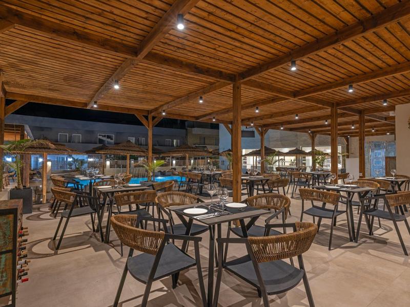 Overdekt buitenterras van een restaurant met tafels en stoelen onder een verlicht houten dak.
