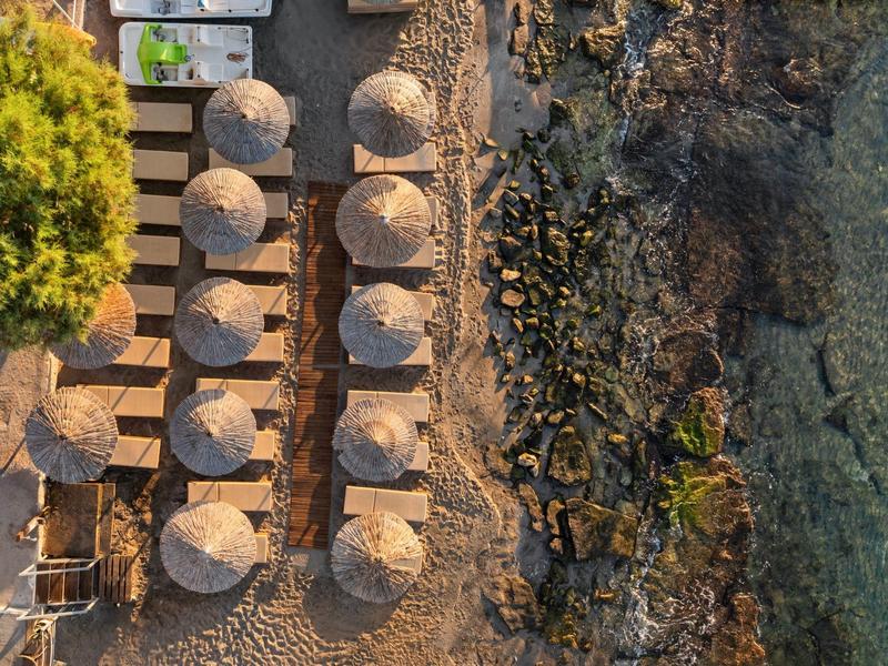 Luchtfoto van een strand met stroparasolletjes en stenen bij het water