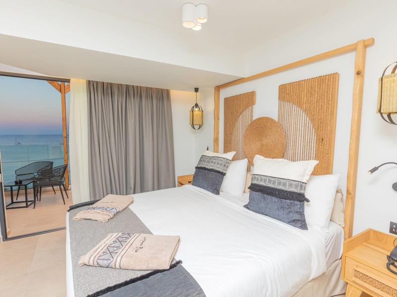 Moderne hotelkamer met tweepersoonsbed en balkon met uitzicht op zee bij zonsondergang.