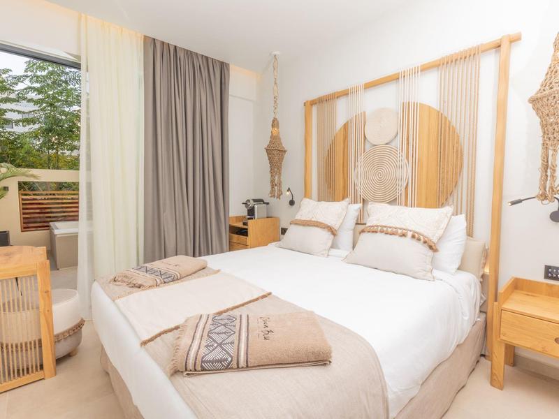 Lichte slaapkamer met tweepersoonsbed, houten meubels en toegang tot een terras met groen uitzicht.