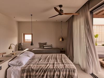 Modernes Schlafzimmer mit großem Bett, hängender Lampe, Ventilator und Zugang zu Terrasse hinter Vorhängen.