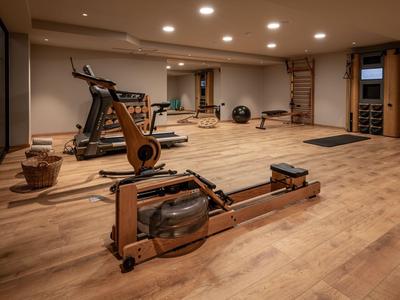 Moderner Fitnessraum mit Holzlattenboden, Rudergerät, Laufband und weiteren Trainingsgeräten.