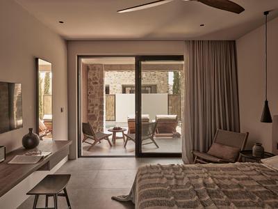 Gemütliches Schlafzimmer mit Bett, Sessel, Vorhängen und Blick auf Terrasse mit Stühlen und Tisch.