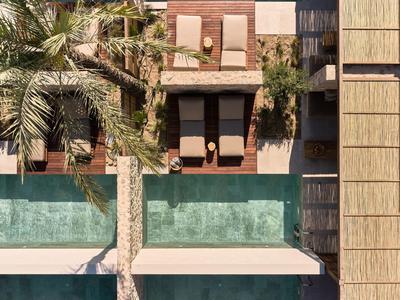 Zwei nebeneinanderliegende Pools mit Liegestühlen und Palmen, umgeben von Holz- und Steinflächen.