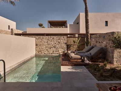 Moderner Garten mit kleinem Pool, zwei Liegestühlen, Steinmauer und hellen Wänden im Hintergrund.