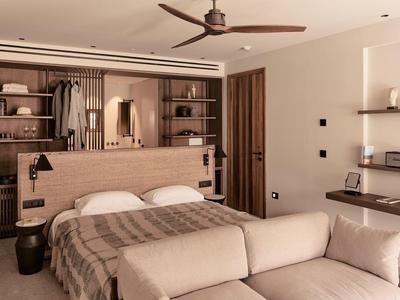 Modernes Schlafzimmer mit hellbraunem Holz, Doppelbett, großer Regalwand und beiger Couch im Vordergrund.