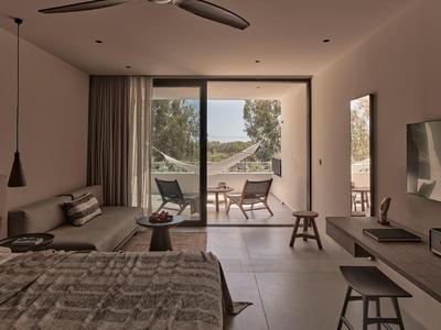 Moderner Hotelraum mit großem Fenster, Doppelbett, Couchecke und Blick auf Terrasse und Meer.