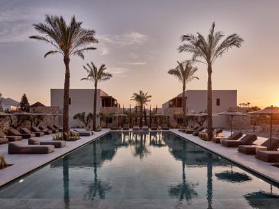 Moderner Pool mit Palmen, Sonnenliegen und Gebäuden bei Sonnenuntergang in entspannter Atmosphäre.