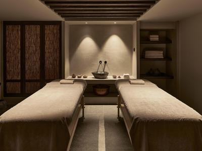 Ein ruhiger Massageraum mit zwei Liegen, warmem Licht und schlichtem, modernem Design.