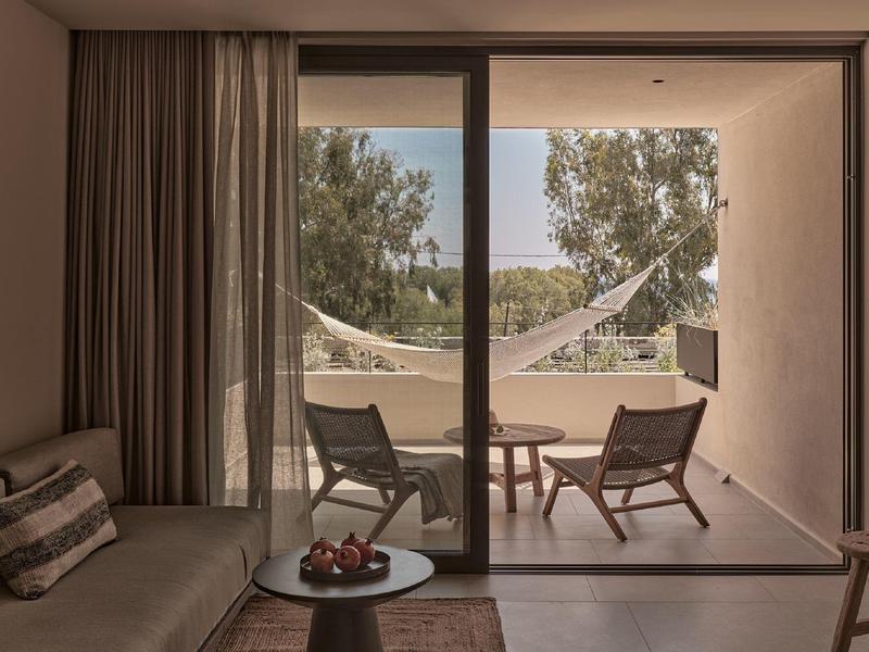 Wohnzimmer mit Sofa, Kissen, Glastisch, zwei Holzstühlen und Hängematte auf der Terrasse.