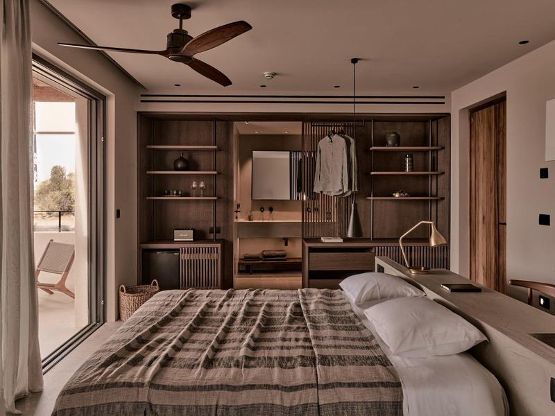 Schlafzimmer mit großem Bett, Holz-Regalen, Schrank, Deckenventilator und Zugang zum Balkon.