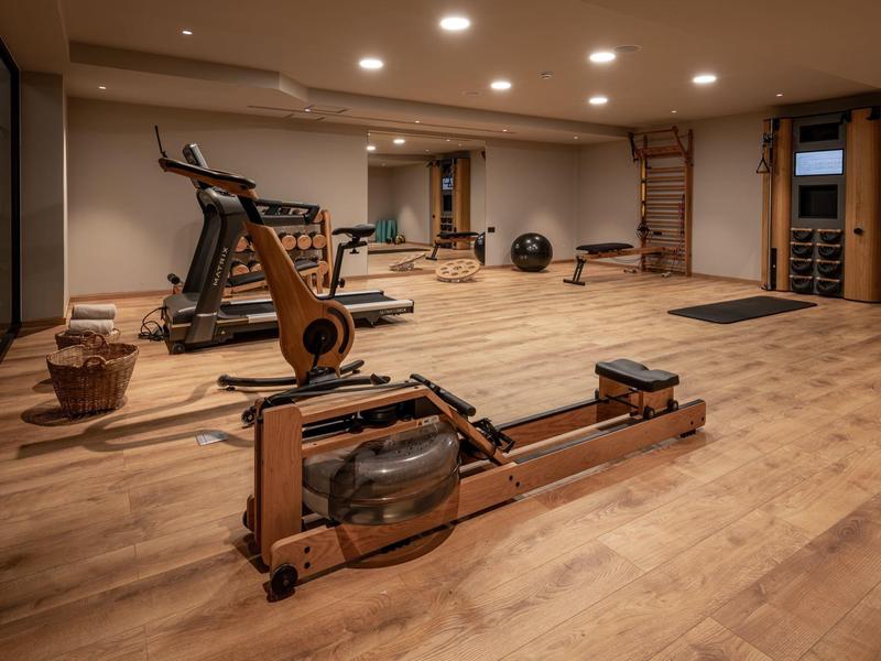 Großer Fitnessraum mit Holzfußboden, Rudergerät, Laufband und anderen Trainingsgeräten.