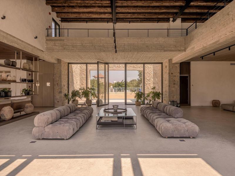 Großes Wohnzimmer mit Betonboden, zwei grauen Sofas, Glaswand und Holzbalkendecke.