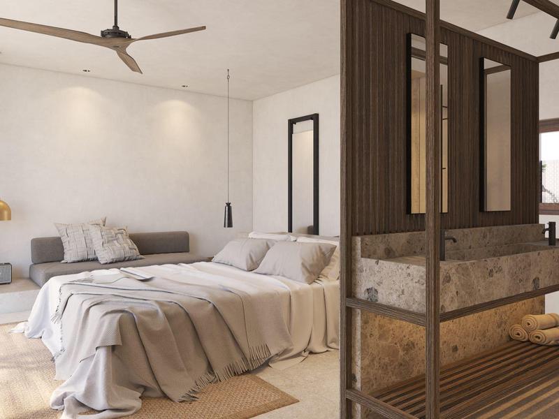 Hell eingerichtetes Schlafzimmer mit weißer Bettwäsche, grauem Sofa und Holzraumteiler mit Sitzbank.