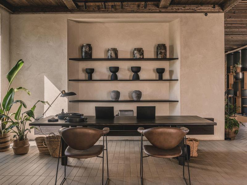 Modernes Büro mit Holzdecke, Pflanzen, großer schwarzer Tisch und drei Stühlen in schlichtem Design.