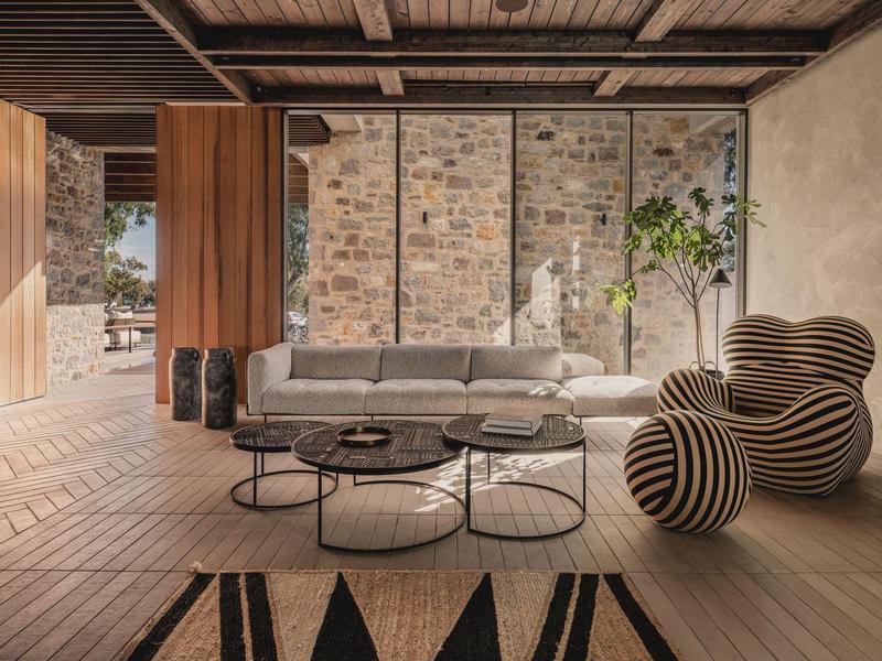 Modernes Wohnzimmer mit grasem Sofa, rundem Couchtisch, gestreiftem Sessel und Steinwand im Hintergrund.