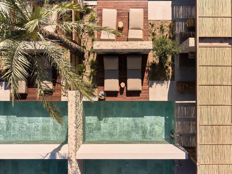 Zwei nebeneinanderliegende Pools mit Liegestühlen und Palmen, umgeben von Holz- und Steinflächen.