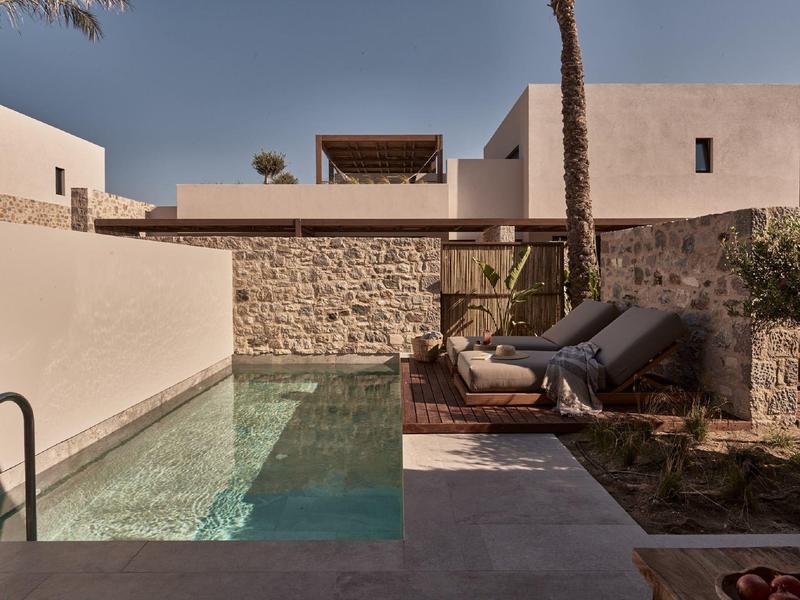 Moderner Garten mit kleinem Pool, zwei Liegestühlen, Steinmauer und hellen Wänden im Hintergrund.