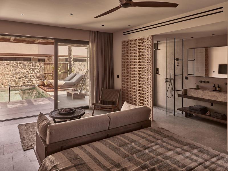 Modernes Schlafzimmer mit Glaswand, angrenzendem Bad und Terrasse mit Pool im warmen Farbton.