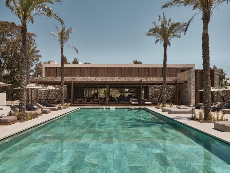 Moderner Pool mit türkisfarbenem Wasser, umgeben von Palmen und loungigen Sonnenliegen.