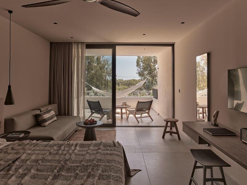 Moderner Hotelraum mit großem Fenster, Doppelbett, Couchecke und Blick auf Terrasse und Meer.