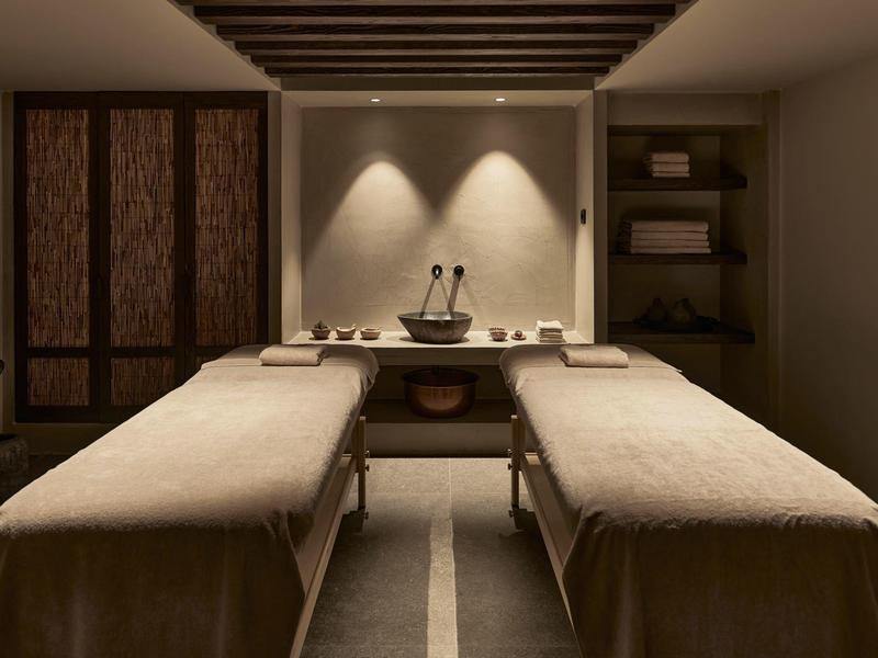 Ein ruhiger Massageraum mit zwei Liegen, warmem Licht und schlichtem, modernem Design.