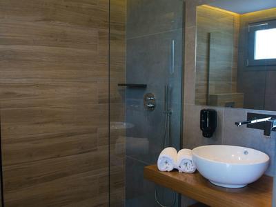 Moderní koupelna se skleněným sprchovým koutem, dřevěnými stěnami a kulatým umyvadlem na dřevěném stole.