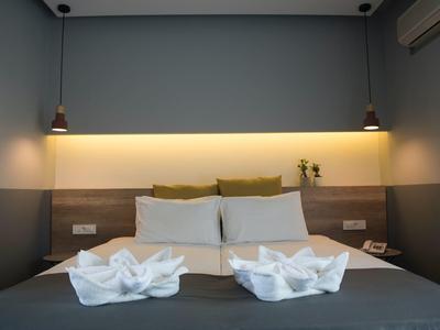 Jednoduše zařízený hotelový pokoj s manželskou postelí, dekoračními ručníky a nepřímým osvětlením.