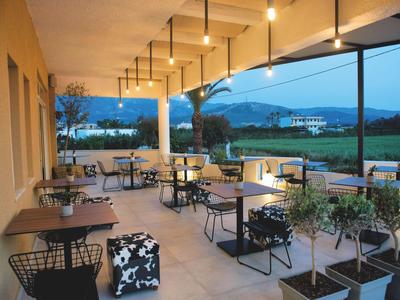 Überdachte Terrasse mit Tischen, Stühlen und Blick auf Landschaft und Berge bei Abenddämmerung.