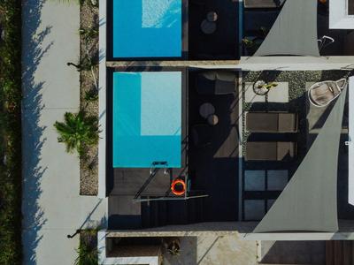 Pohled z ptačí perspektivy na moderní dům s modrým bazénem a venkovním posezením.