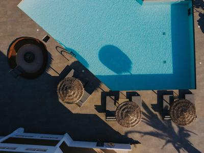 Vogelperspektive eines Schwimmbeckens mit Sonnenschirmen und Liegestühlen neben einem Hotel.