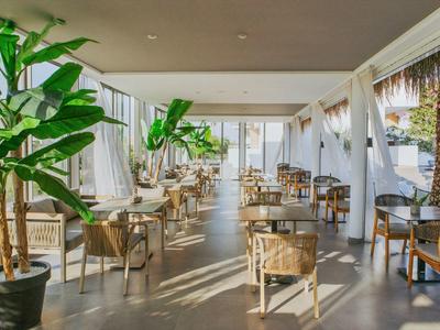 Elegantní venkovní prostor hotelu s stoly, židlemi a zelenými rostlinami pod zastřešenou střechou.