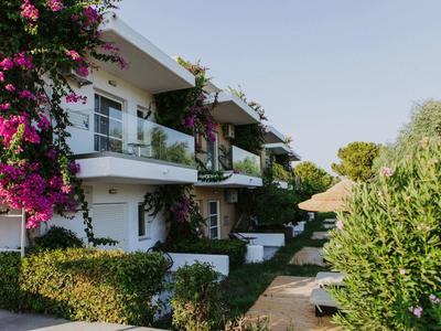 Moderní hotelový komplex s balkony, bílými zdmi a kvetoucími rostlinami na slunném místě.