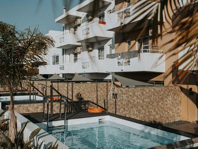 Moderner Hotelpool im Freien mit Palmen und weißem Gebäude im Hintergrund.