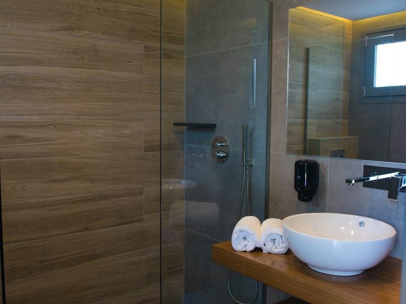 Moderní koupelna se skleněným sprchovým koutem, dřevěnými stěnami a kulatým umyvadlem na dřevěném stole.