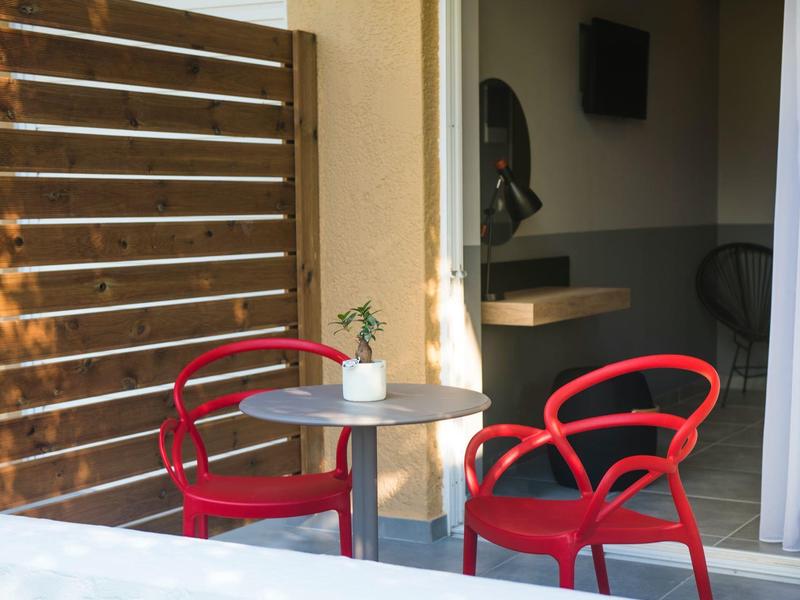 Dva červené židle a kulatý stůl na balkóně s výhledem do pokoje.