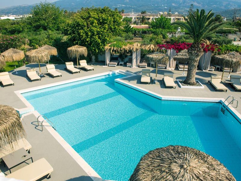 Velký venkovní bazén s lehátky a palmami v tropickém hotelovém areálu.