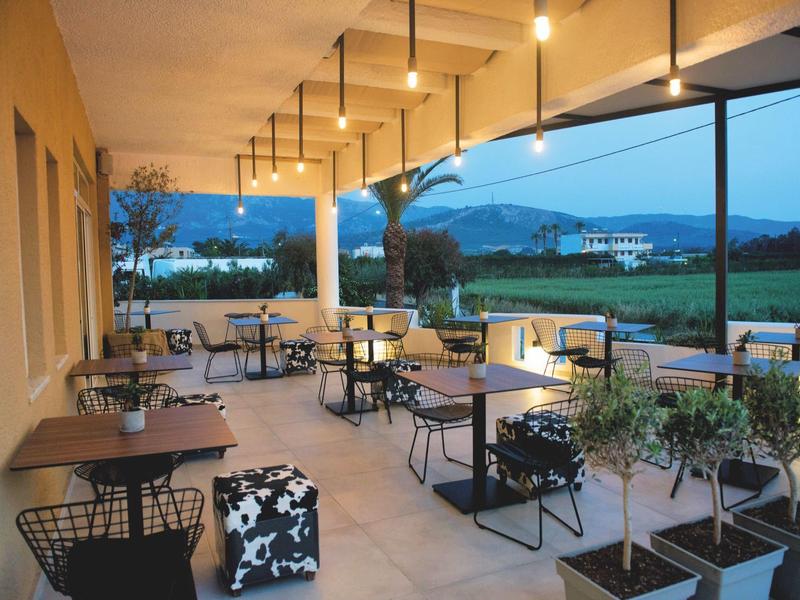 Otevřená terasa s stoly, židlemi a výhledem na krajinu za soumraku.